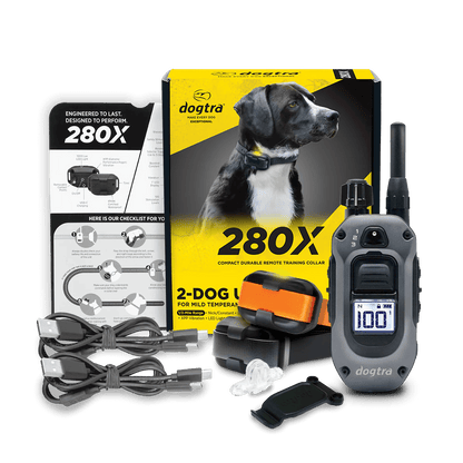 Dogtra 280X 2-dog remote training collar kit displayed with full contents. Includes product box featuring a black and white dog, remote transmitter with digital display, two color-coded receiver collars (orange and black), dual charging cables, test light tool, user manual, and quick-start guide. Designed for training mild temperament dogs.